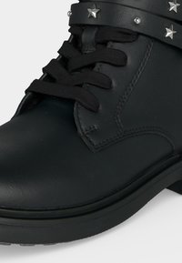 Bottine en cuir noir avec lacets noirs, bride décorative cloutée ornée de clous argentés en forme d'étoile et talon bas.