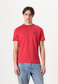 Rød bomull T-skjorte med korte ermer, rund hals og marineblå logo med tallet 4. Bært sammen med lyseblå jeans.