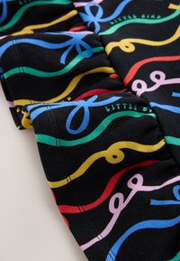 Tissu noir avec des lignes ondulées colorées en bleu, vert, rouge, jaune et rose, avec des coutures froncées et un texte partiel « LITTLE B ».