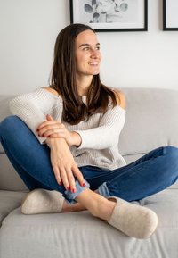 Graue Wollclogs mit abgerundeten Zehen und einer natürlichen Holzsohle, getragen mit blauen Jeans, die an den Bündchen aufgerollt sind; der Pullover hat ein schulterfreies Design.