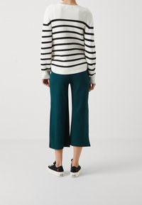 Stribet striktrøje i hvid og sort, parret med teal ribbede culotter og sorte sneakers med hvide såler og kirsebærfarvede accenter.