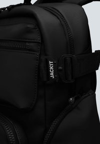 Zaino nero realizzato in materiale sintetico liscio. Dotato di una tasca con zip, tracolla regolabile con fibbia in plastica e cucitura a contrasto.