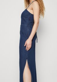 Robe maxi en denim avec bretelles ajustables, fente sur le côté et accents de perles colorées sur la bretelle, mettant en avant un corsage ajusté et une silhouette en A.