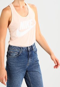 Rosa ärmlös linne med en stor vit Nike-logotyp, i kombination med högmidjade blå denimjeans med en urtvättad finish.