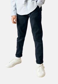 Tengerészkék chinos egyenes szárú kialakítással, felhajtott mandzsettákkal és sima pamut anyagból, fehér tornacipőkkel párosítva.