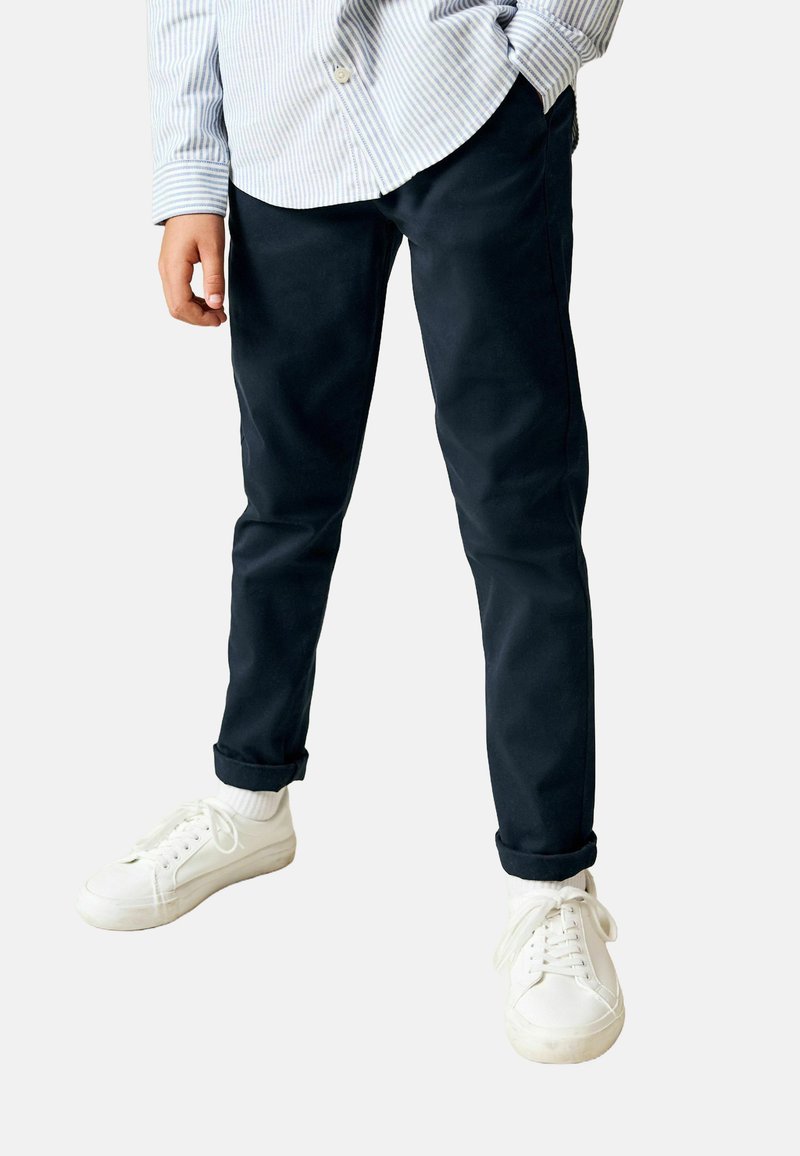 Tengerészkék chinos egyenes szárú kialakítással, felhajtott mandzsettákkal és sima pamut anyagból, fehér tornacipőkkel párosítva.