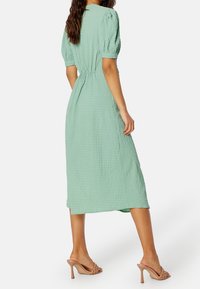 Mintgrön puffärmad klänning i texturerat tyg, midi-längd med en figursydd midja, med mjuka veck och rund halsringning.