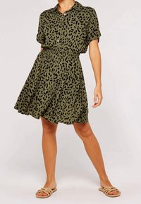 Kortærmet, grøn skjortekjole med sort leopardprint, figursyet talje og flared nederdel. Båret med beige slid-sandaler, der viser et afslappet look.