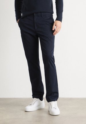 Pantaloni in cotone blu navy a taglio dritto, con tasche laterali e una texture liscia, abbinati a sneaker bianche.