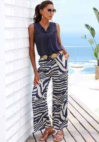 Navy blue sleeveless top with lace accents, paired with wide-leg pants in beige and navy zebra stripes, complemented by a metallic belt and sandals.
