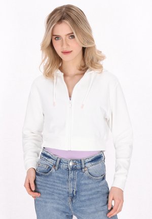 Weißer, kürzer geschnittene Kapuzenpullover mit einem Reißverschluss auf der Vorderseite, Kordelzug und langen Ärmeln, kombiniert mit hochgeschnittenen hellblauen Jeans. Glatte Stoffoberfläche.