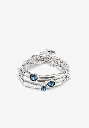 Bracelet en argent sterling avec un design enroulé, comportant trois pierres précieuses rondes de couleur bleue. Des perles texturées créent un aspect superposé.