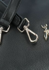 Borsa a mano in pelle nera con accessori in metallo silver, compresi una clip e un ciondolo decorativo. Superficie texturizzata con dettagli sulle cinghie.