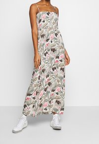Robe longue à fines bretelles, motif floral en rose et vert, tissu léger, associée à des baskets blanches pour un look décontracté.