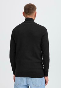 Svart genser med høy hals, lange ermer og ribbestrikket kant. Laget av et mykt materiale, med en ensfarget overflate.