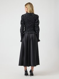 Μαύρη μπλούζα με πουά σχέδιο, φουσκωτά μανίκια και ρελιασμένη υφή, συνδυασμένη με κομψή μαύρη σατέν φούστα. Συνολικά μια κομψή σιλουέτα.