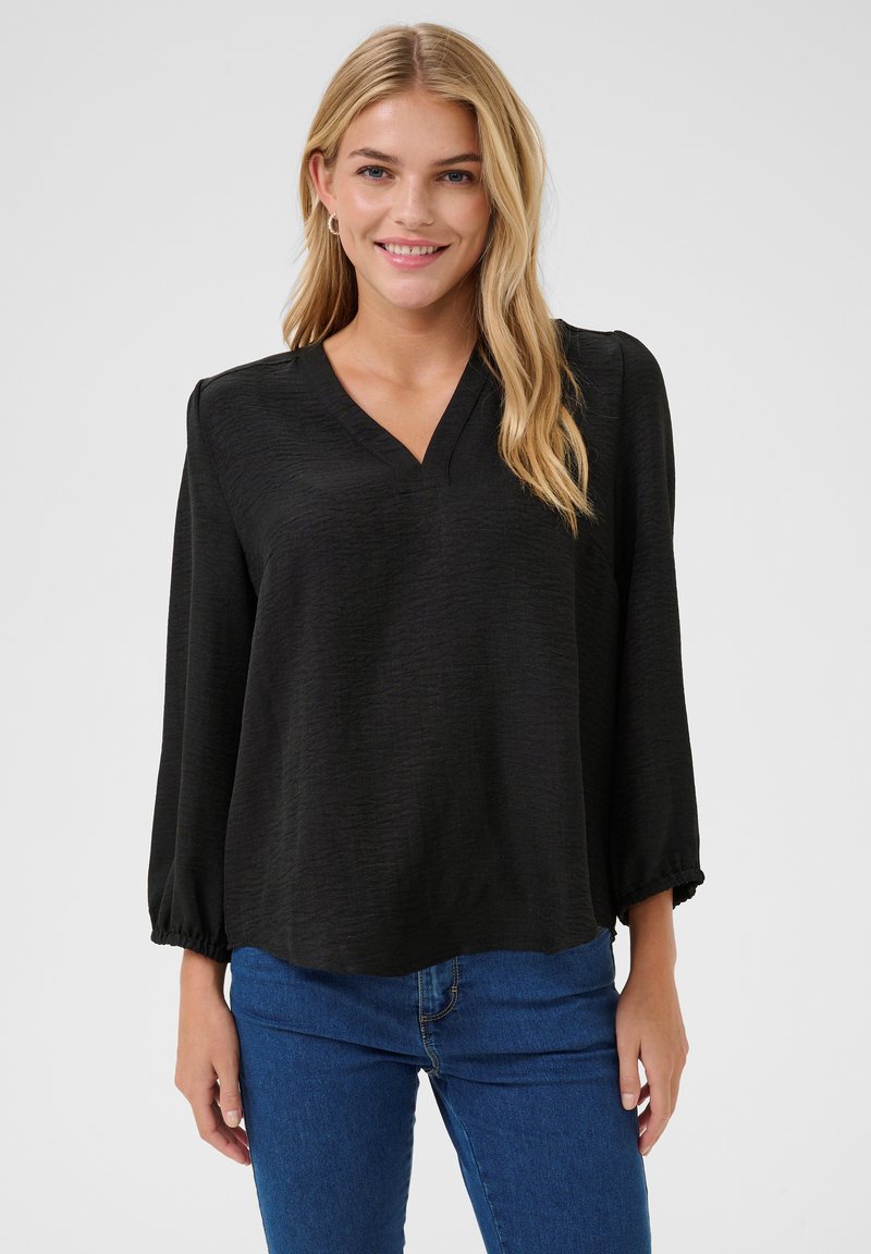 Black blouse with a V-neckline, long sleeves with elastic cuffs, and a textured fabric. Paired with blue denim jeans.