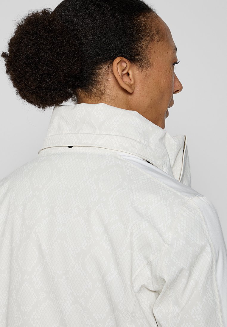 Weißer Blazer mit dezentem Schlangenprintmuster. Hoher Kragen, glatte Textur und Reißverschluss. Verfügt über kontrastierende Schulterakzente.