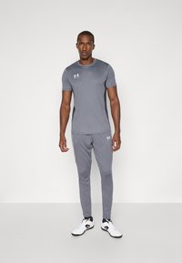 Grå trenings T-skjorte og matchende bukser laget av lett materiale. Har hvite logo-detaler og en slim fit-design. Svart og hvite treningssko.