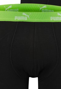 Schwarze Boxer-Briefs mit einem grünen elastischen Bund, der ein weißes "Puma"-Logo trägt, aus glattem Stoff und mit Flachnähte für Komfort.