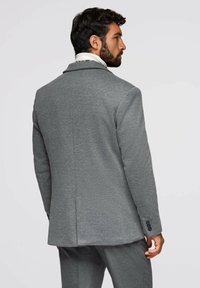 Grå skräddarsydd blazer i mjukt tyg, med klassisk kavajkrage, strukturerade axlar och detaljer med treknappsmuddar.