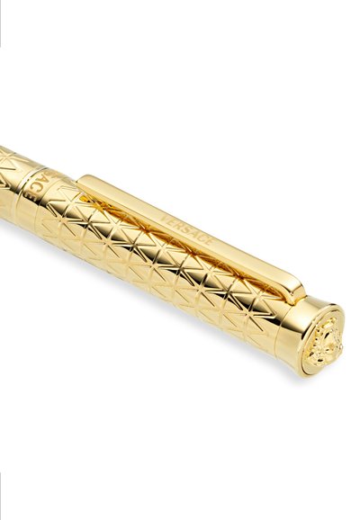 Bolígrafo dorado con una superficie texturizada que presenta un patrón de diamantes y un emblema de león en la tapa, con la marca "VERSACE" en el clip.