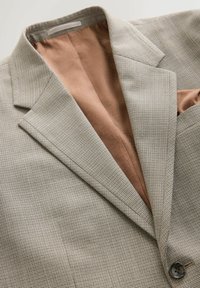 Blazer beige de pata de gallo con solapa con muesca, un botón y forro interior marrón con estampado; cuenta con un bolsillo en el pecho.