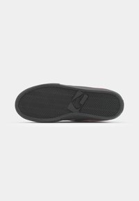Shoe outsole featuring a textured black rubber surface with a zigzag pattern and a small triangular logo detail. Designed for grip and durability.
