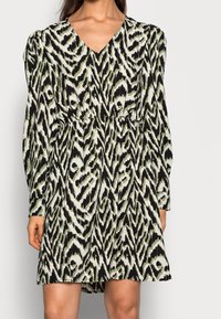 Long-sleeved dress featuring a black, white, and green ikat pattern, with a V-neckline and an elastic waist for a fitted silhouette.
