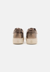 Sneakers in bronzo con una finitura in pelle lucida, caratterizzati da una suola spessa di colore crema e una chiusura a cerniera. Logo "Tamaris" impresso sul tallone.