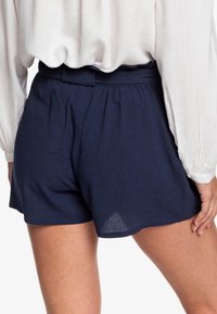 Granatowe szorty o luźnym kroju z paskiem w talii i plisami. Wykonane z lekkiego materiału o gładkiej strukturze.