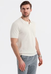 Kortærmet polo skjorte i off-white strikstof med et struktureret mønster, ribbet krave og kant, parret med grå stribede bukser.