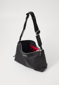 Borsa a mano in pelle nera con chiusura a zip. Presenta una tracolla removibile e un interno rosso brillante con il marchio "HUGO" visibile.