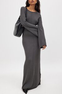 Robe tricotée grise longue avec un col rond et des manches évasées, dotée de coutures verticales. Associée à un sac à main noir et des chaussures à bout pointu.