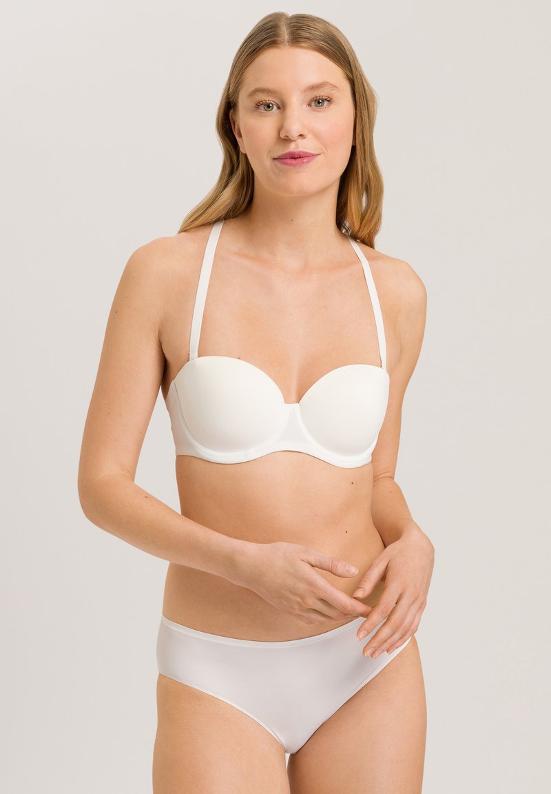 Bílý formovaný podprsenkový šálek s nastavitelnými ramínky, hladkým povrchem a bezšvovým designem. V kombinaci s odpovídajícími bílými bikini kalhotkami, minimalistický styl.