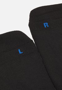 Svarte sokker med ribbet tekstur, merket med blå "L" for venstre og "R" for høyre på den øverste kanten. Enkel og funksjonell design.