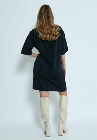 Zwarte oversized jurk met korte mouwen, met een relaxte snit en een zachte textuur. Gecombineerd met beige leren laarzen tot de knie.