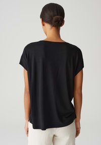 Zwarte top met korte mouwen, gemaakt van een gladde stof, met een relaxte pasvorm, brede halslijn en zijsplitten aan de zoom.