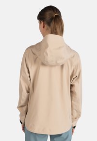 Beige vattenavvisande jacka med huva, som har en avslappnad passform, elastiska manschetter och en slät yta. Bakvyn visar sömdetaljer och logotyp.