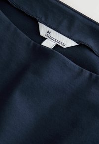 Nærbillede af mørkeblå stof med et hvidt mærke syet ind i kraven, der står "N. PREMIUM COLLECTION."