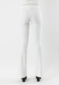 Pantaloni bianchi a zampa d'elefante realizzati in tessuto elastico; presentano una vita alta, aderenti sulla coscia e si allargano dal ginocchio. Scarpe con piattaforma nere.