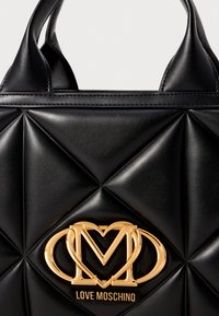 Black quilted handbag made of synthetic leather featuring a prominent gold-tone logo and geometric embossed pattern.