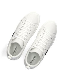 Witte sneakers met een gestructureerd krokodillenpatroon, ronde neus, witte veters en een achtertab. Merken zijn zichtbaar op de binnenzool.