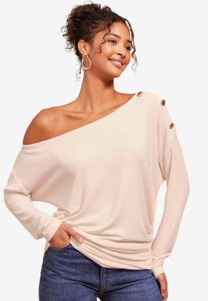 Světlá růžová top off-the-shoulder s dlouhými rukávy, zdobený třemi zlatými knoflíky na jednom rameni, jemná textura a volný střih.