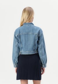 Light blue denim jacket with a cropped design, button closure, and long sleeves. Features a pointed collar and visible stitching details.