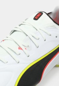 Scarpa da calcio bianca con dettagli testurizzati in nero e giallo. Presenta una tomaia in mesh, lacci evidenti e il marchio "KING" in rosso.