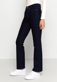 Mørkeblå denim flared jeans med høj talje, fem lommer og orange syninger. Sammen med hvide sneakers.