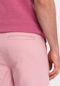 Světle růžové šortky vyrobené z bavlny, s úzkým střihem a zadní kapsou s horizontálním otvorem. Nosit s ležérním růžovým tričkem.