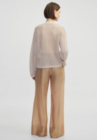Maglione beige chiaro a lavorazione aperta con maniche lunghe e scollatura rotonda, abbinato a pantaloni larghi in leggero marrone chiaro.