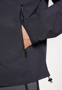 Svart myk skalljakke med lukket lomme, elastiske mansjetter og justerbar hem. Glatt tekstur og minimalistisk design.